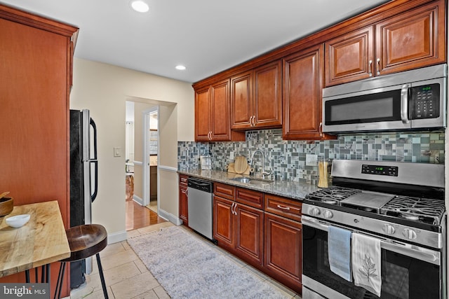 kitchen with light stone counters, tasteful backsplash, appliances with stainless steel finishes, a sink, and baseboards