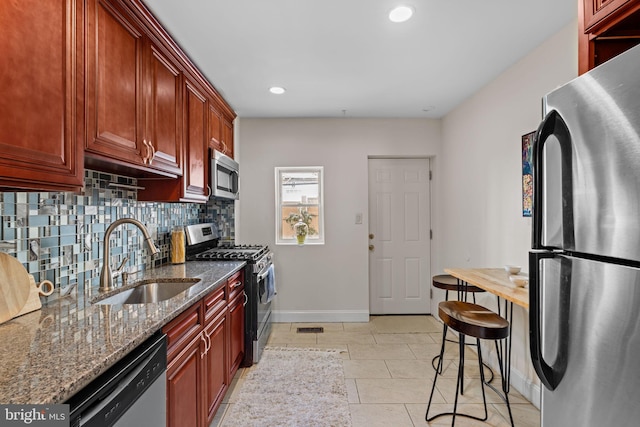 kitchen with stainless steel appliances, backsplash, a sink, dark stone counters, and baseboards