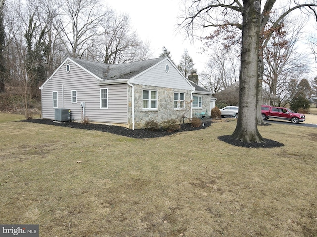 view of side of home featuring stone siding, a yard, a chimney, and central air condition unit