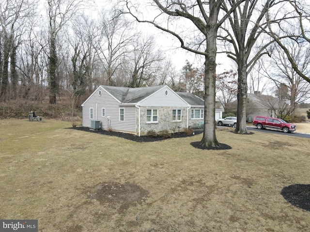 view of front of home with stone siding, central AC unit, and a front lawn