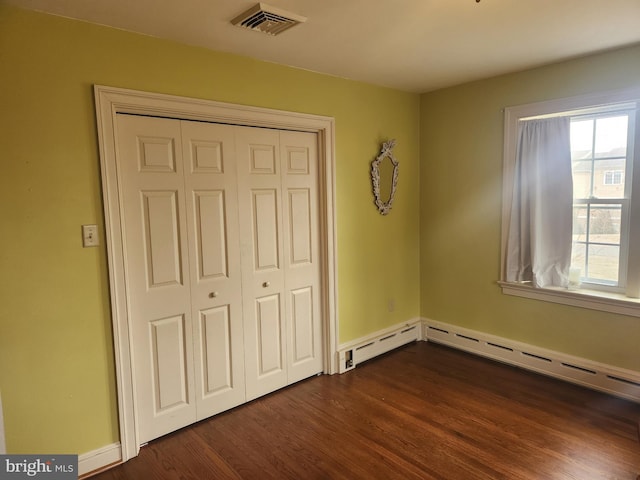 unfurnished bedroom featuring baseboards, visible vents, dark wood-type flooring, baseboard heating, and a closet