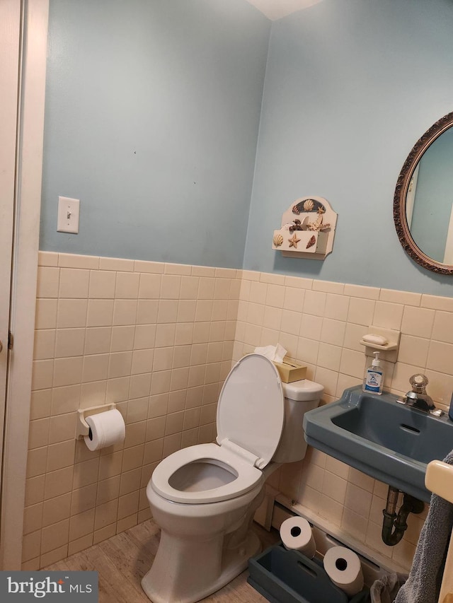 bathroom with wood finished floors, a sink, toilet, and tile walls