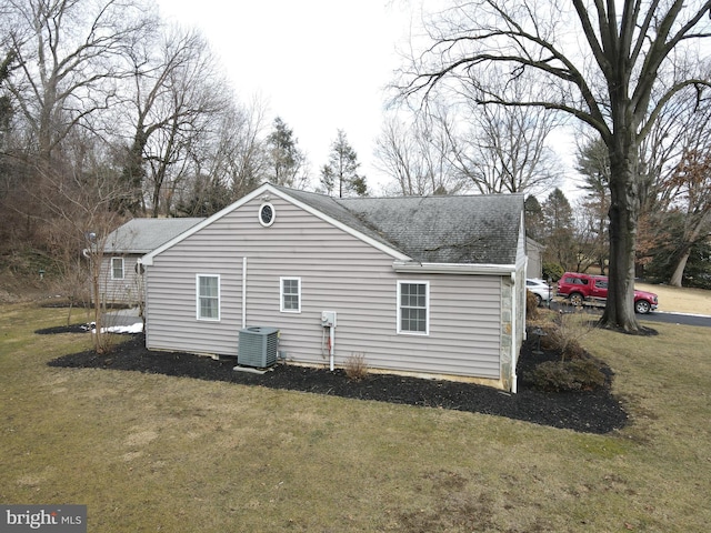 back of property featuring central AC unit, a lawn, and roof with shingles