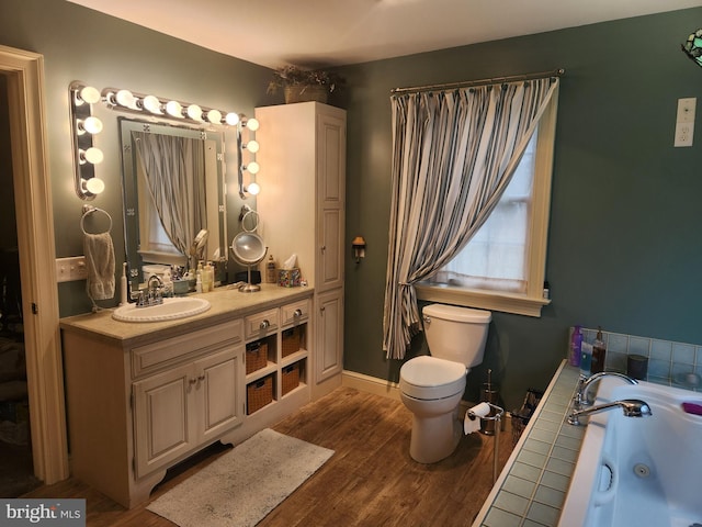 bathroom with baseboards, toilet, a tub with jets, wood finished floors, and vanity