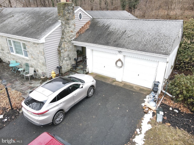 view of front of house featuring a shingled roof, stone siding, a chimney, and a garage