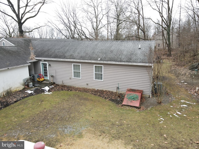 exterior space featuring cooling unit, roof with shingles, and a lawn