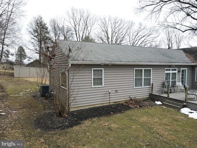 rear view of house featuring roof with shingles, a lawn, central AC unit, fence, and a wooden deck