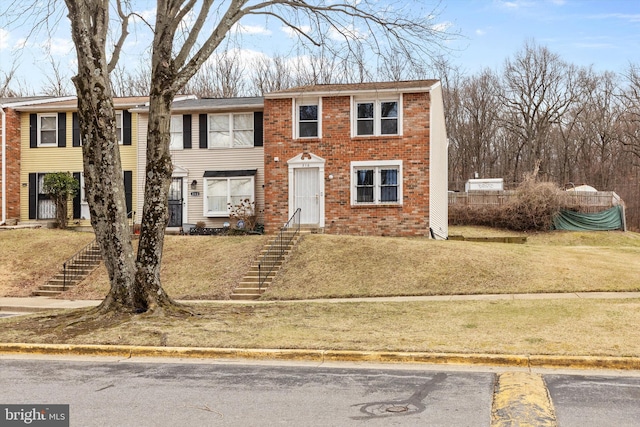 townhome / multi-family property featuring brick siding, a front lawn, and stairway