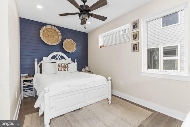 bedroom with an accent wall, recessed lighting, wood finished floors, and baseboards