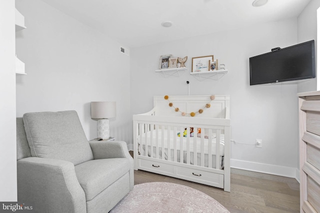 bedroom with a nursery area, visible vents, baseboards, and wood finished floors