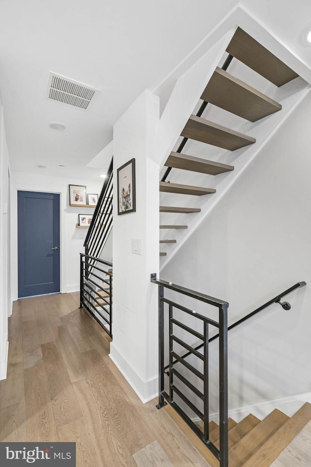 stairway featuring wood finished floors, visible vents, and baseboards