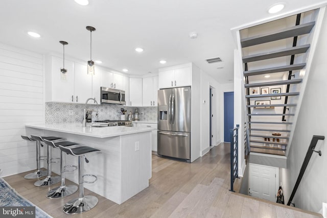 kitchen featuring a breakfast bar area, stainless steel appliances, a peninsula, visible vents, and light wood-type flooring