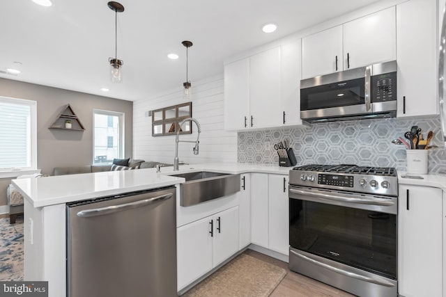 kitchen featuring stainless steel appliances, tasteful backsplash, light countertops, a sink, and a peninsula