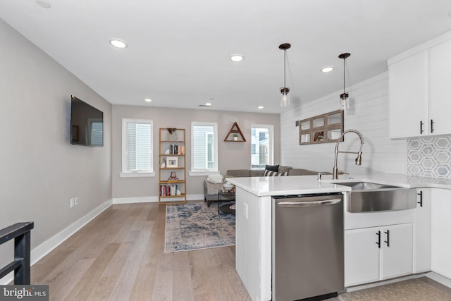 kitchen with light countertops, backsplash, stainless steel dishwasher, a sink, and light wood-type flooring