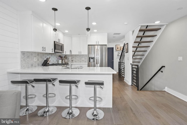 kitchen with a peninsula, wood finished floors, a sink, appliances with stainless steel finishes, and decorative backsplash