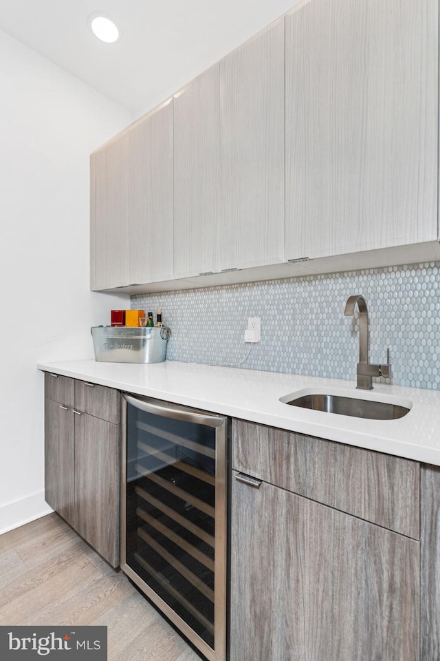 bar with tasteful backsplash, light wood-style floors, a sink, beverage cooler, and baseboards