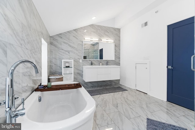 bathroom with lofted ceiling, a freestanding tub, visible vents, and tile walls