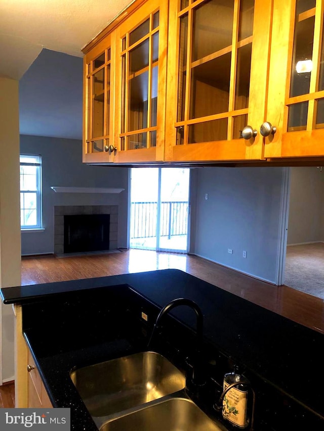 kitchen featuring a tiled fireplace, dark countertops, wood finished floors, and a sink