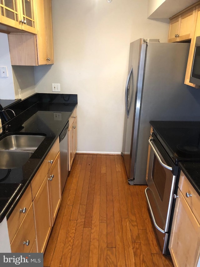 kitchen with dark wood-style floors, dark stone counters, a sink, glass insert cabinets, and appliances with stainless steel finishes