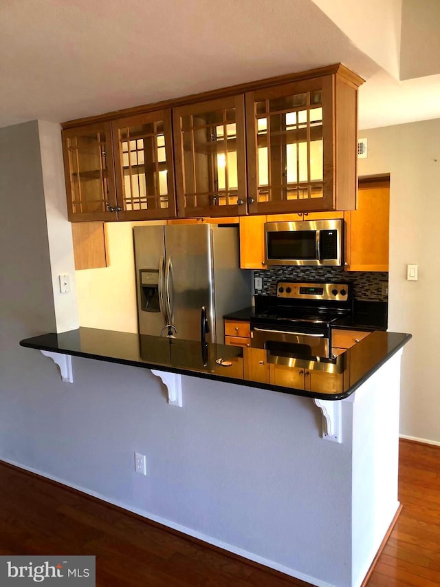 kitchen featuring dark countertops, tasteful backsplash, appliances with stainless steel finishes, a peninsula, and dark wood-style floors