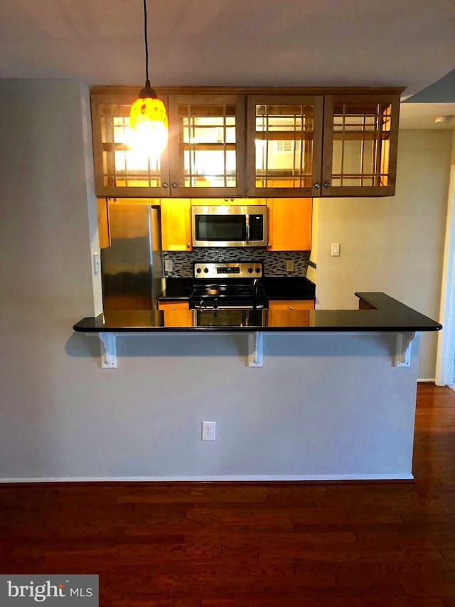 kitchen featuring dark wood-style floors, decorative backsplash, appliances with stainless steel finishes, dark countertops, and a kitchen breakfast bar