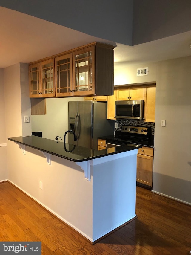 kitchen featuring a kitchen bar, visible vents, dark countertops, dark wood-style floors, and stainless steel appliances