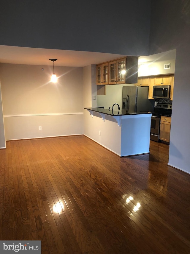 kitchen with dark countertops, appliances with stainless steel finishes, dark wood-type flooring, and a peninsula