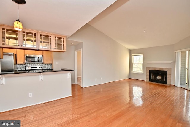 kitchen with light wood-type flooring, dark countertops, stainless steel appliances, a fireplace, and hanging light fixtures