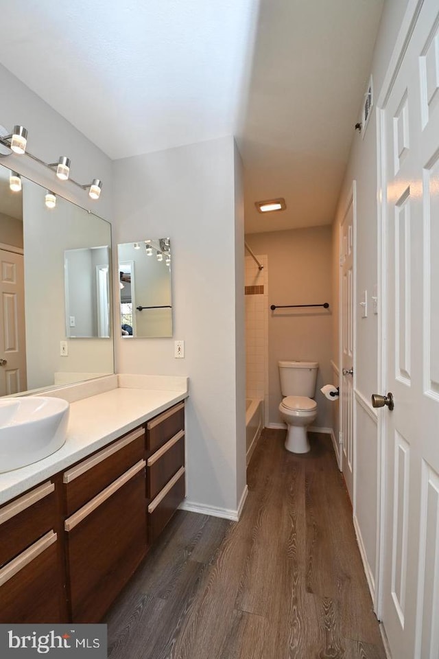 bathroom with baseboards, toilet, shower / tub combination, wood finished floors, and vanity