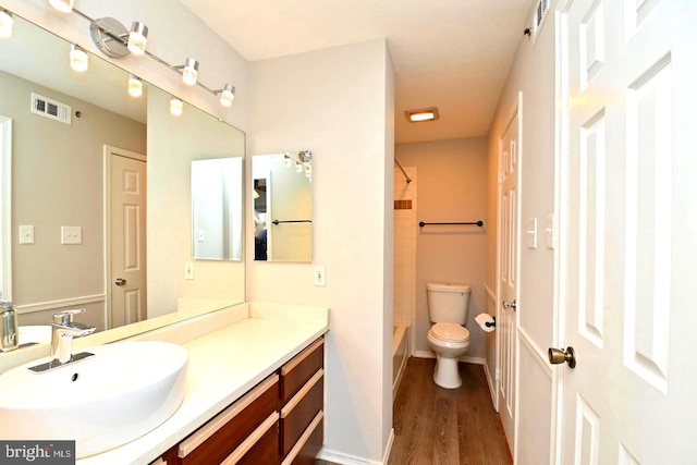 bathroom featuring visible vents, toilet, vanity, wood finished floors, and washtub / shower combination