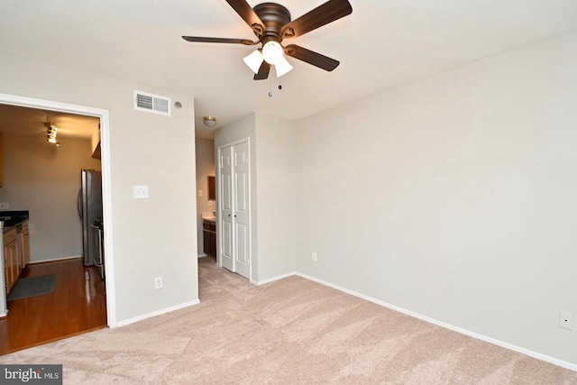 unfurnished bedroom featuring visible vents, baseboards, freestanding refrigerator, a closet, and light carpet