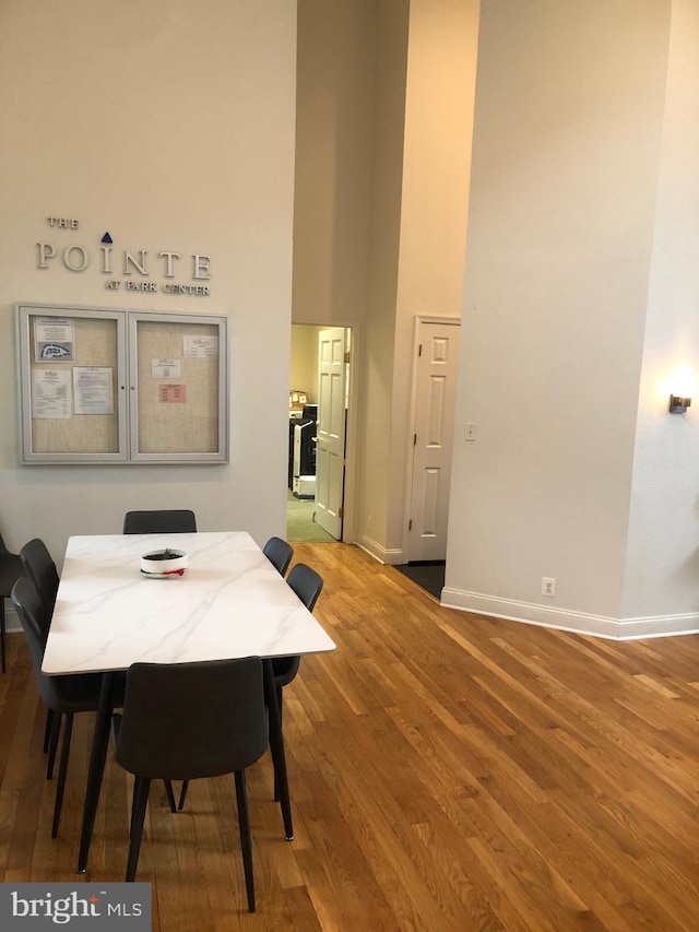 dining space with baseboards, wood finished floors, and a towering ceiling