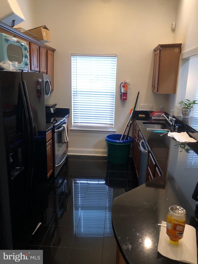 kitchen with dark tile patterned floors, a sink, dark countertops, appliances with stainless steel finishes, and baseboards