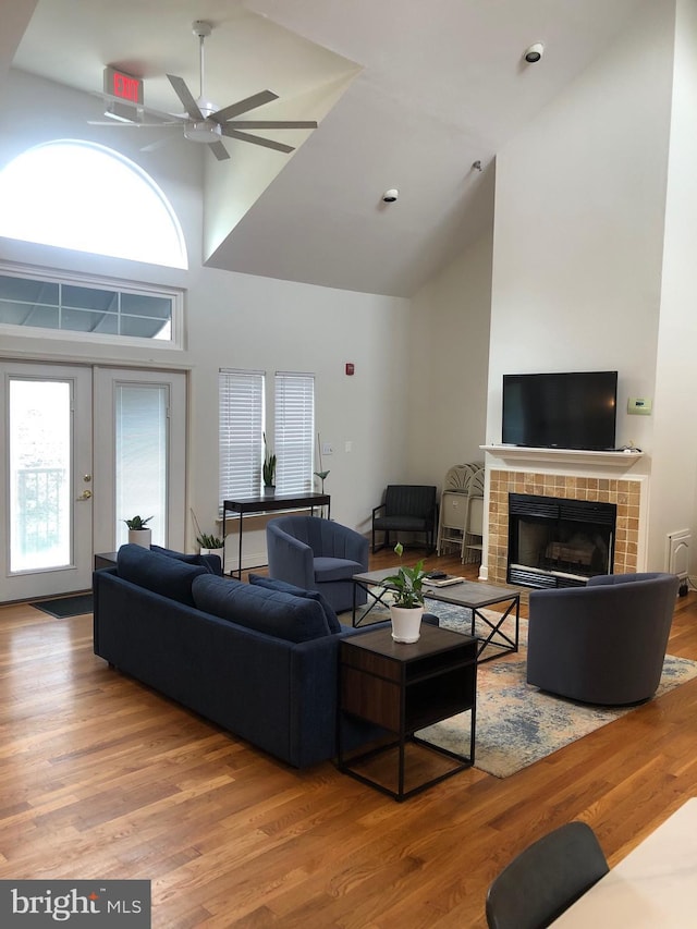 living area with wood finished floors, high vaulted ceiling, a fireplace, ceiling fan, and french doors