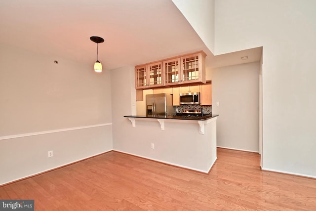 kitchen featuring a kitchen bar, tasteful backsplash, stainless steel appliances, light wood finished floors, and glass insert cabinets