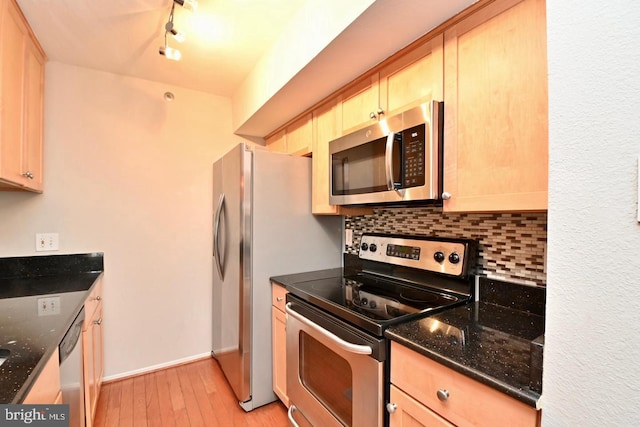 kitchen with dark stone countertops, backsplash, stainless steel appliances, light wood-style floors, and baseboards