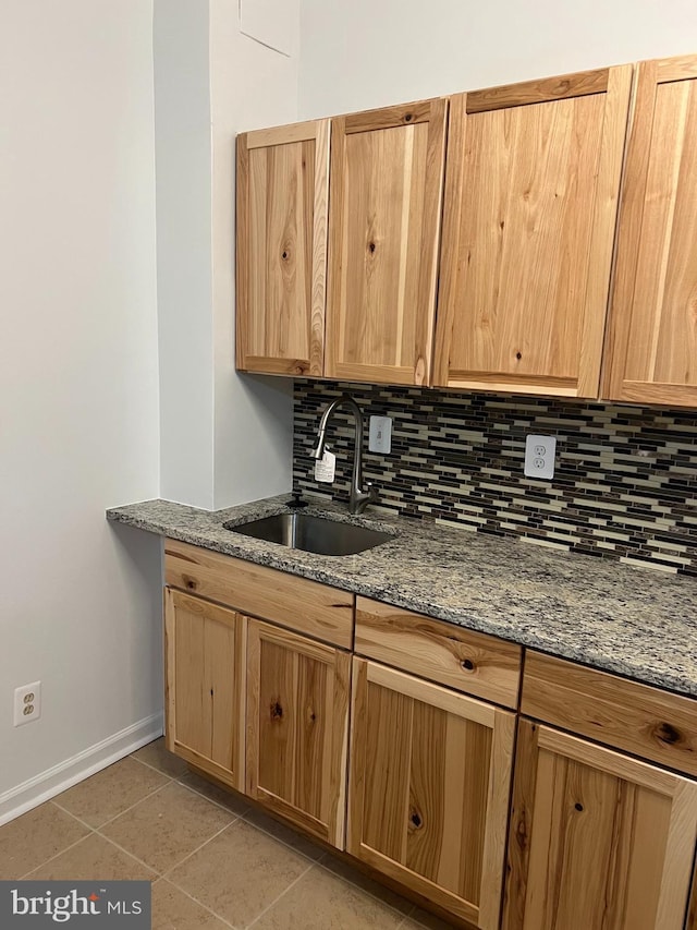 kitchen with stone countertops, light tile patterned flooring, a sink, and decorative backsplash