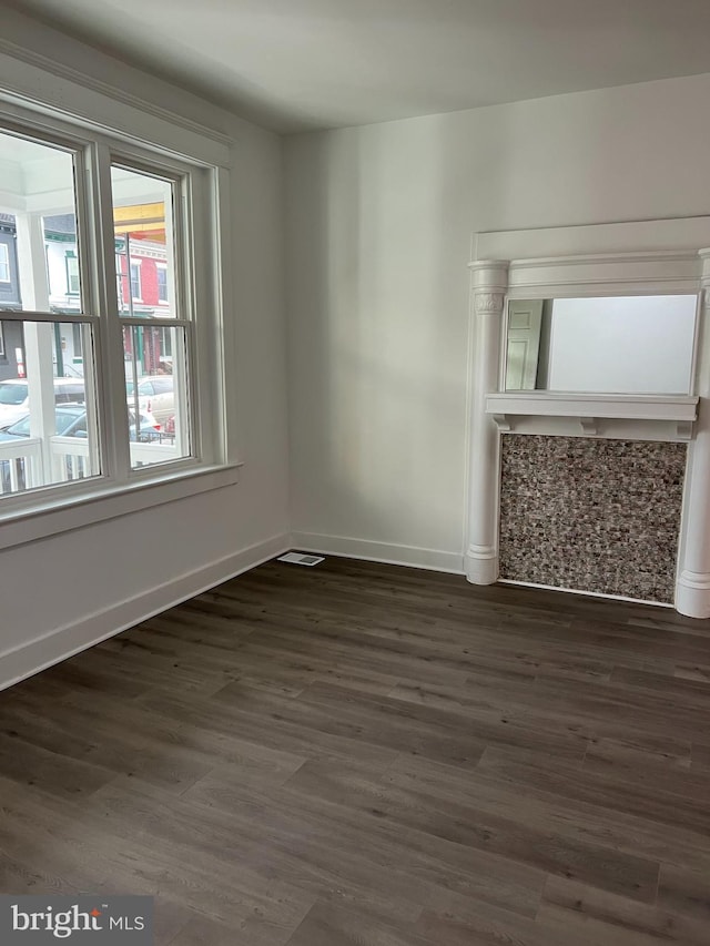 empty room with dark wood-type flooring, visible vents, and baseboards