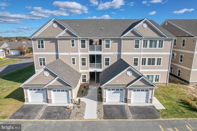 multi unit property featuring a shingled roof, a front lawn, a residential view, a balcony, and driveway