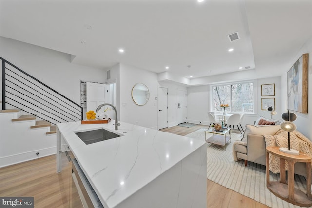 kitchen with light wood finished floors, visible vents, an island with sink, light stone counters, and a sink