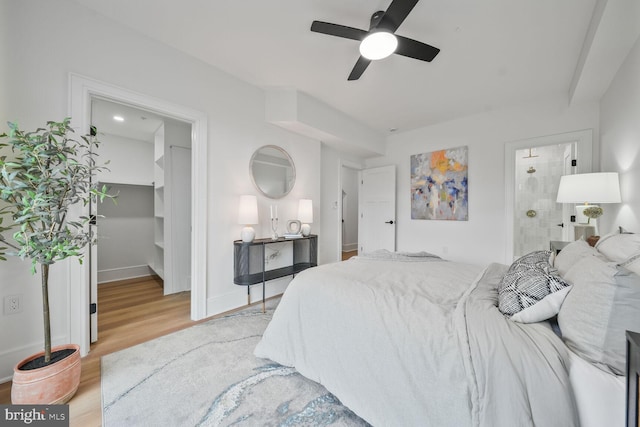 bedroom featuring ceiling fan, baseboards, light wood-style floors, a spacious closet, and ensuite bath