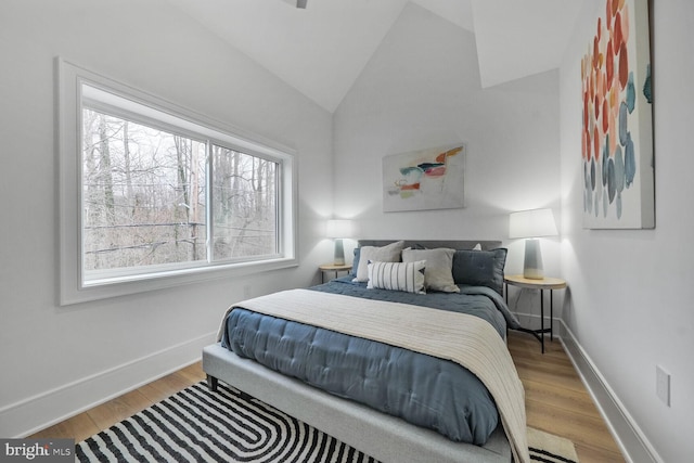 bedroom with light wood-type flooring, vaulted ceiling, and baseboards