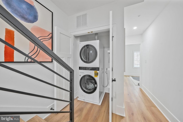 laundry room with laundry area, stacked washer and dryer, wood finished floors, visible vents, and baseboards