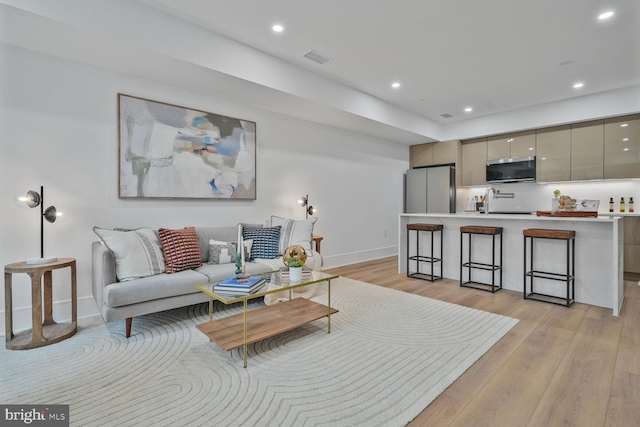 living room featuring light wood-style floors, recessed lighting, visible vents, and baseboards