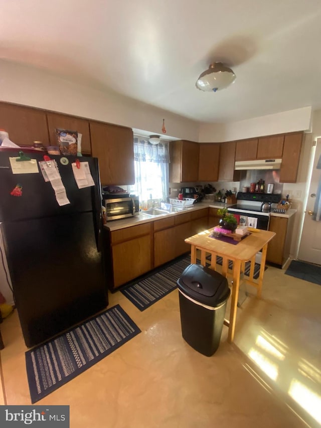 kitchen featuring brown cabinetry, a toaster, freestanding refrigerator, a sink, and under cabinet range hood