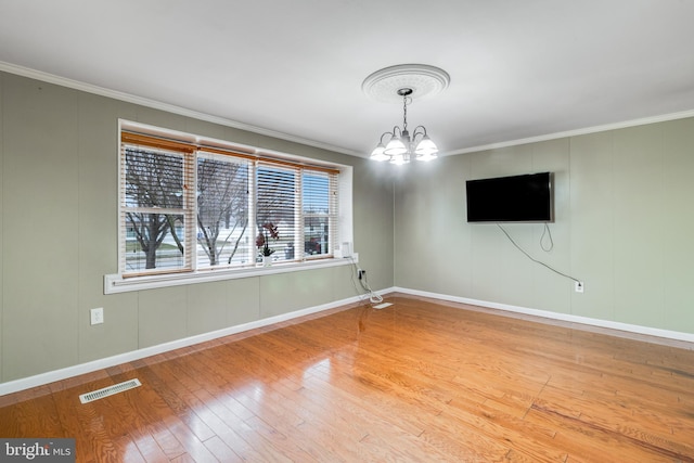 spare room featuring baseboards, visible vents, ornamental molding, hardwood / wood-style flooring, and a chandelier