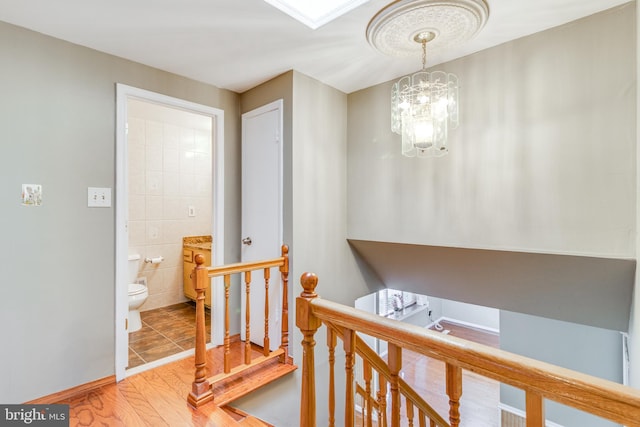 hallway featuring tile walls, an upstairs landing, light wood-style floors, and a chandelier