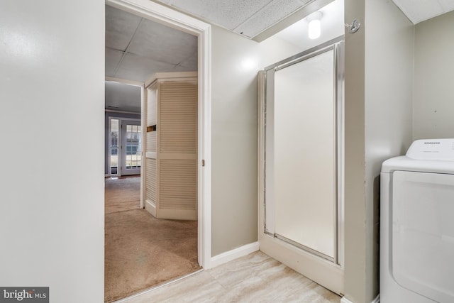 bathroom featuring a paneled ceiling, washer / clothes dryer, baseboards, and a stall shower