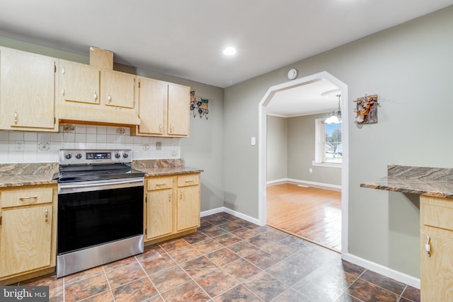 kitchen with electric stove, under cabinet range hood, arched walkways, decorative backsplash, and baseboards