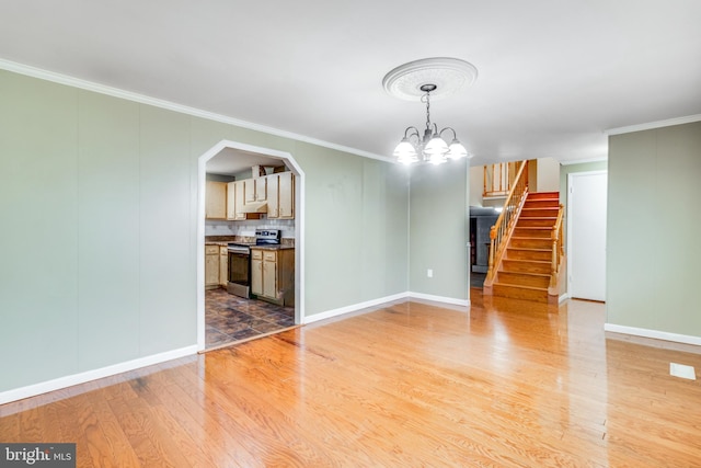 unfurnished living room featuring light wood finished floors, stairway, arched walkways, and crown molding